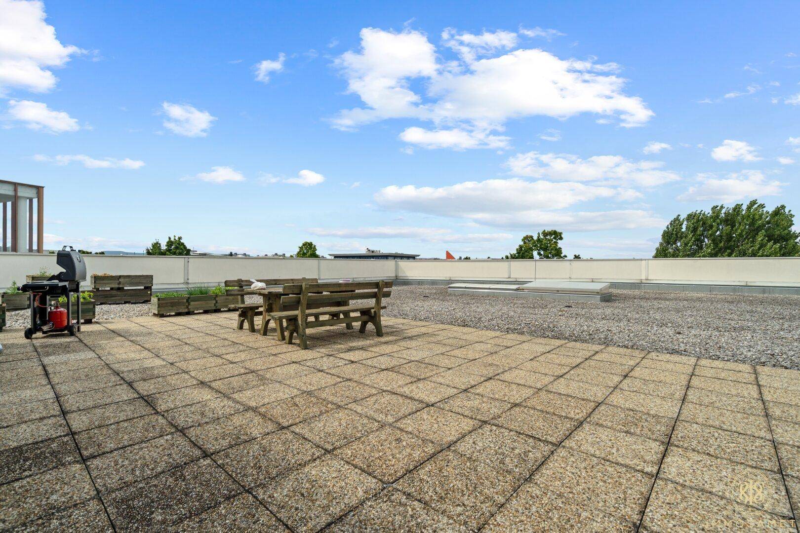 Große Dachterrasse mit Steinplatten, Sitzgelegenheiten und Grill, ideal für Pausen im Freien und Entspannung.