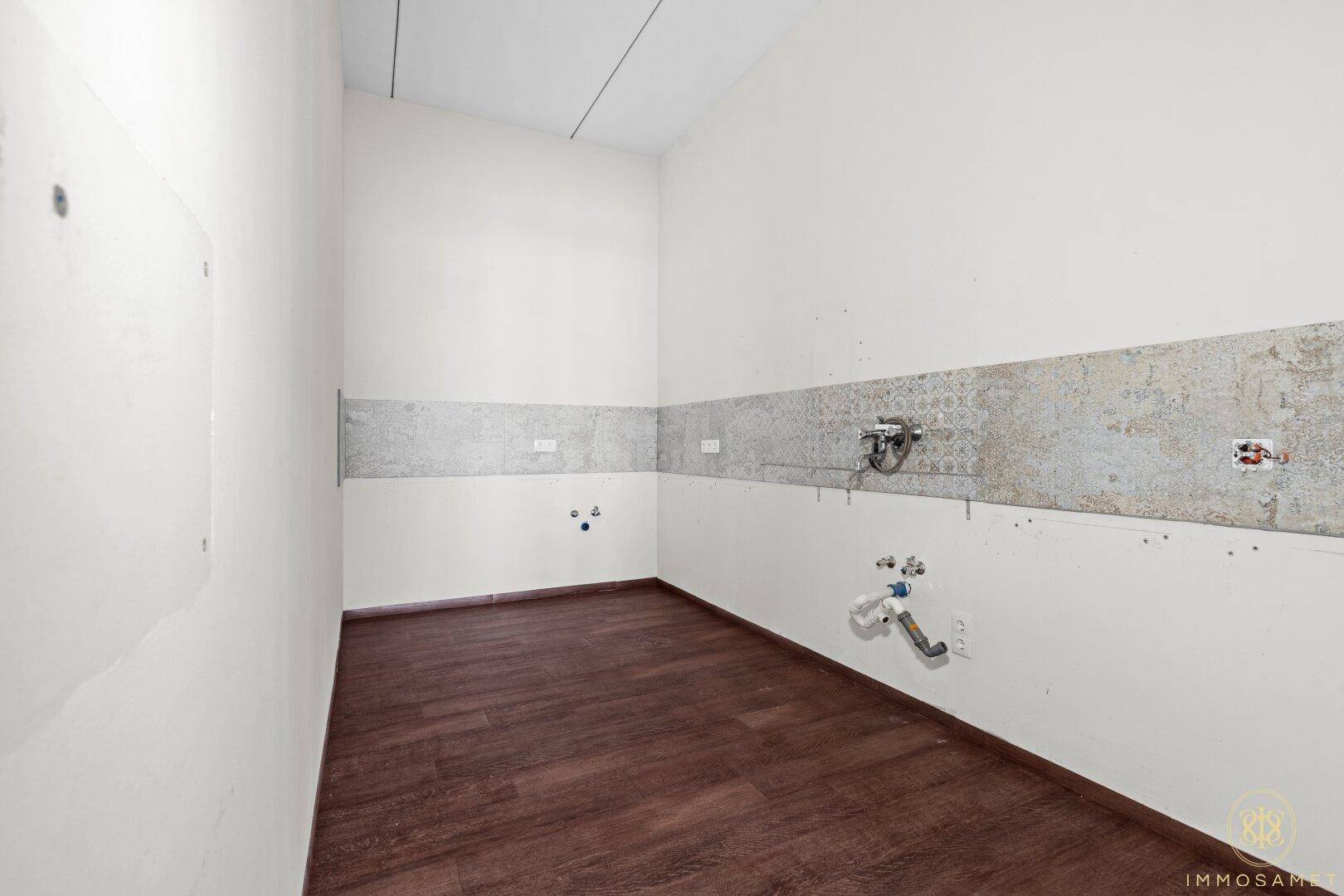Kleiner Raum für eine Küchenzeile mit Holzoptikboden und vorbereiteten Anschlüssen, bereit zur Installation.