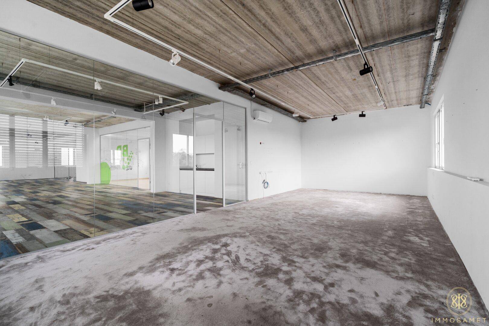 Moderner Büroraum mit Holzboden, Glaswänden und Sichtbetondecke.