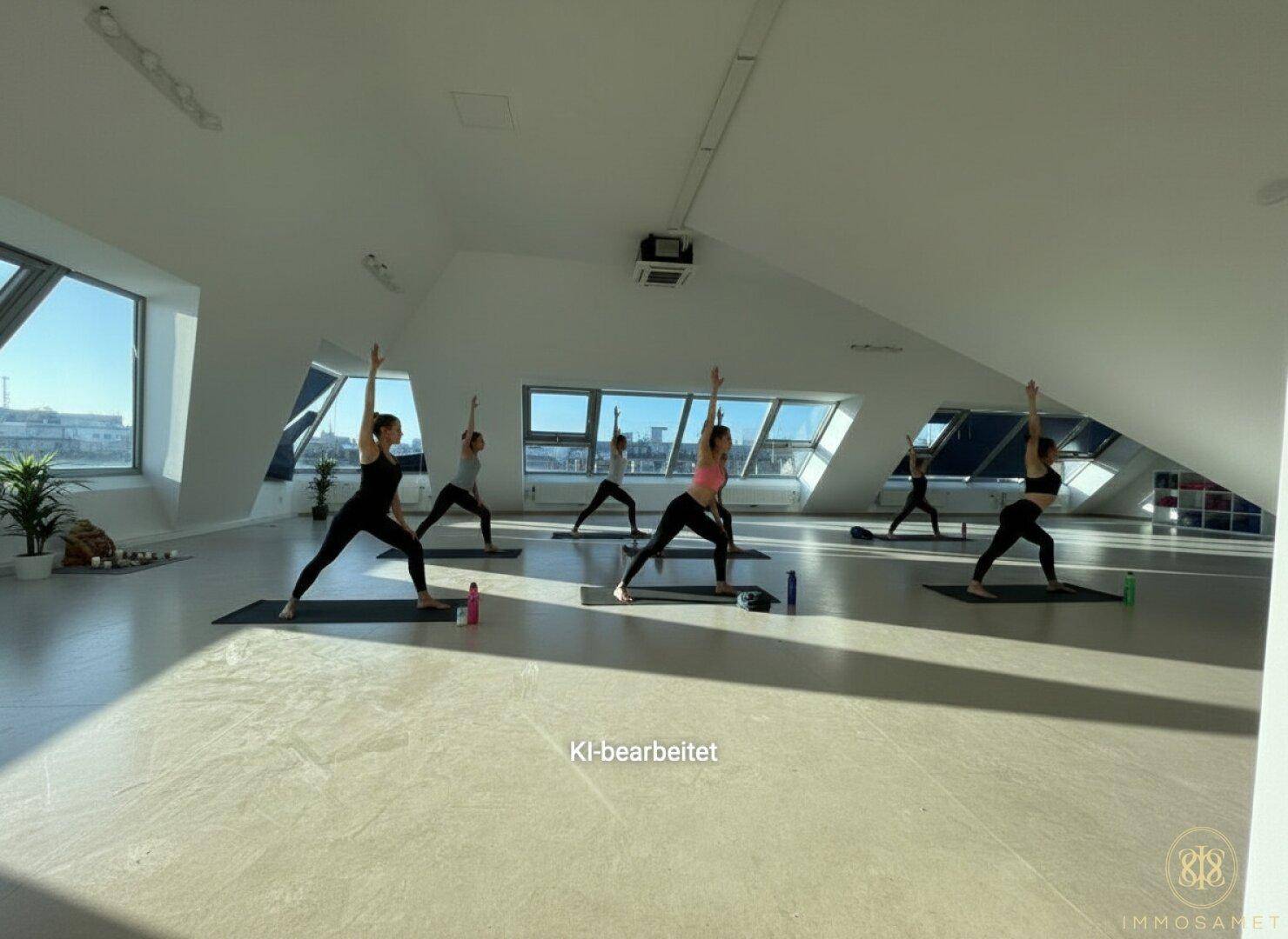 Heller Dachgeschossraum, genutzt als Yogastudio, mit großen Fenstern und Blick auf die Stadt.