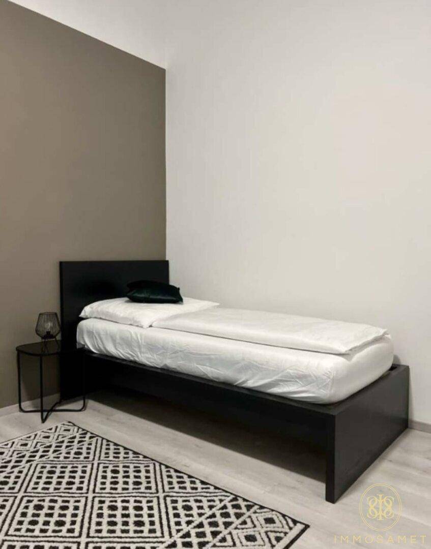 Einzelnes Schlafzimmer mit modernem Bett, Teppich und einer stilvollen Akzentwand.