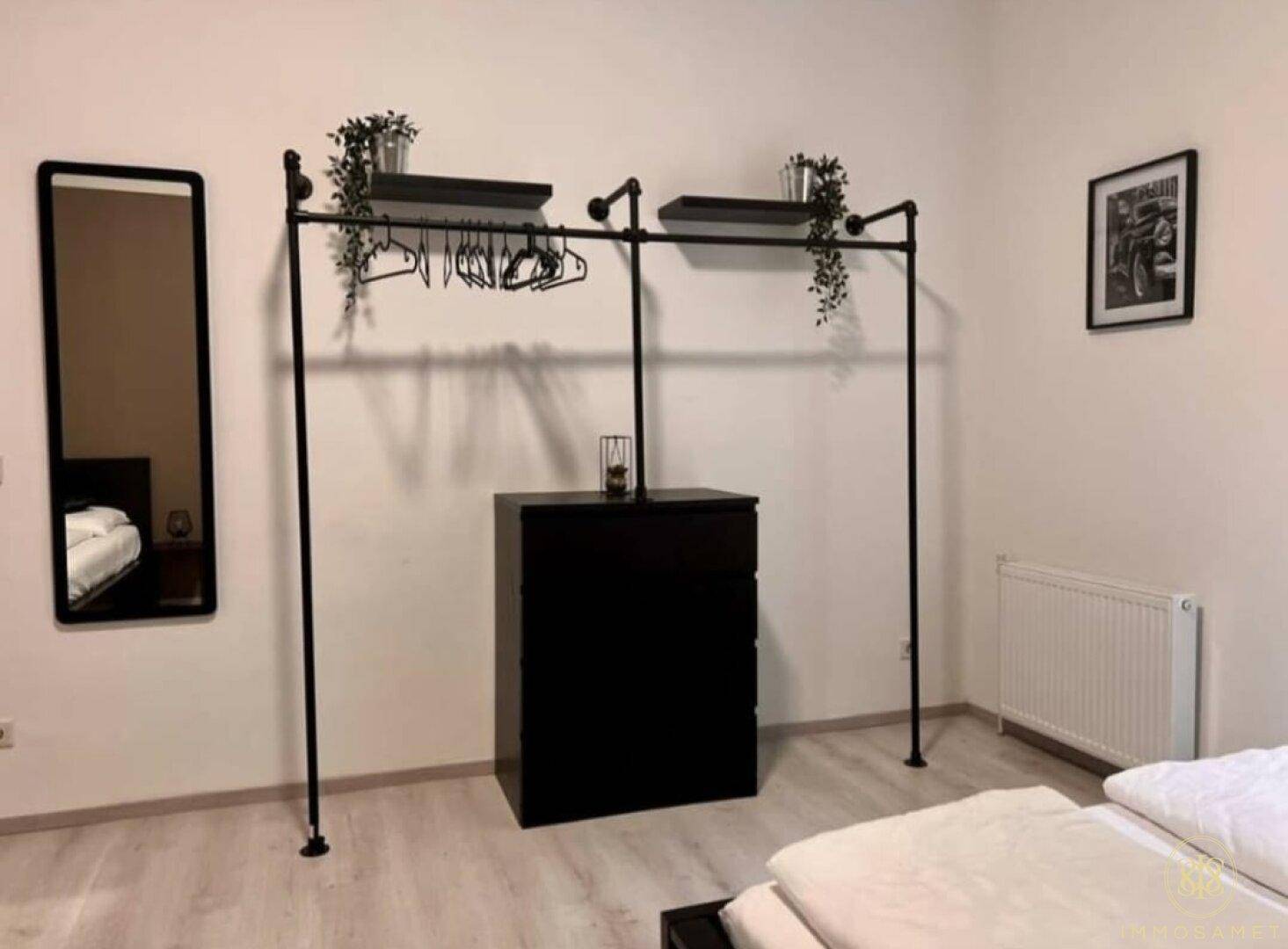 Schlafzimmer mit praktischem offenem Kleiderschrank-System, großem Spiegel und Heizkörper.