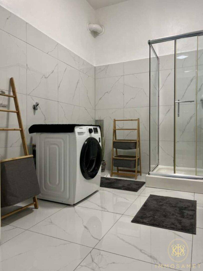 Geräumiges Badezimmer mit Duschkabine, Waschmaschine und eleganten Marmor-Fliesen.