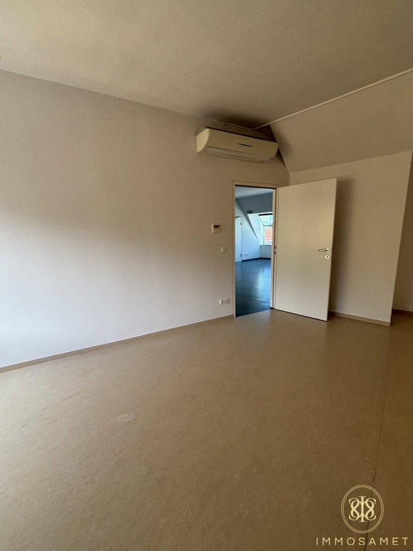 Geräumiger, heller Raum mit Klimaanlage und beigem Bodenbelag, mit Zugang zu einem weiteren Zimmer.
