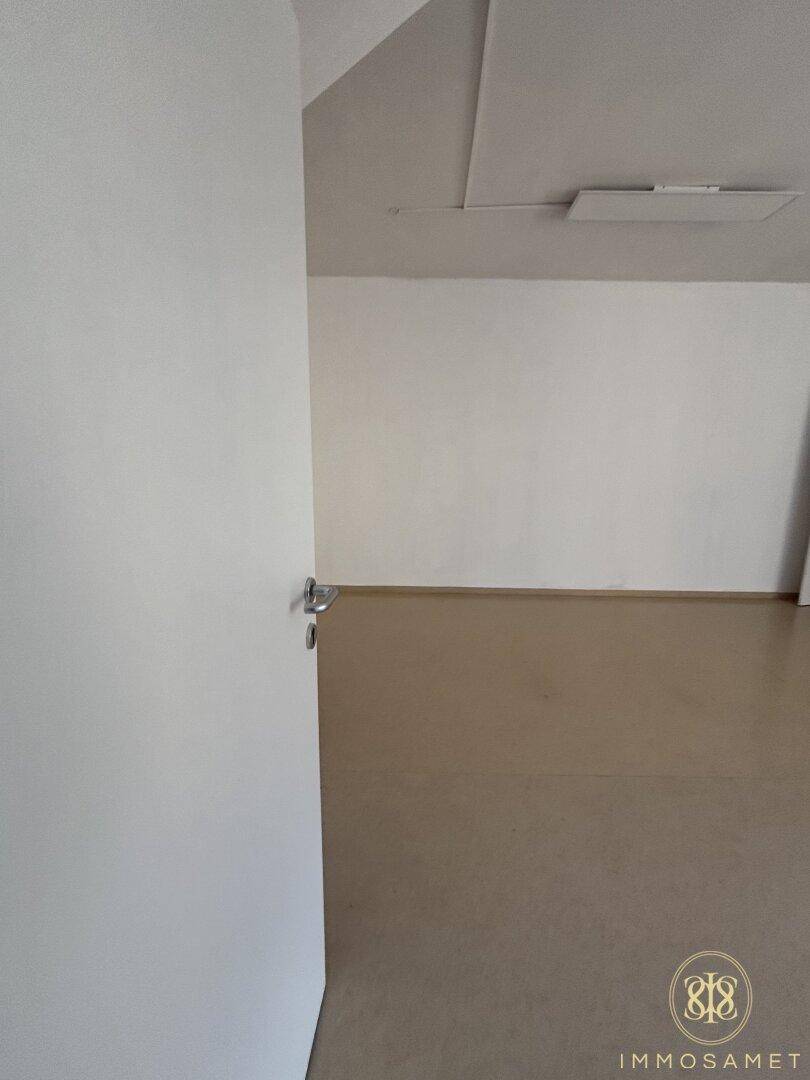 Leerer Raum mit hellem Bodenbelag und weißen Wänden, teilweise mit Dachschräge, bietet viel Potenzial.
