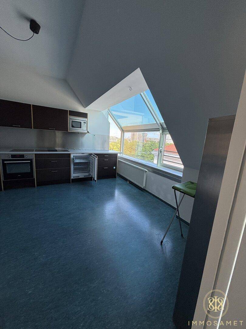 Moderne Küche im Dachgeschoss mit dunklen Schränken, Einbaugeräten und großem Fenster mit Ausblick ins Grüne.