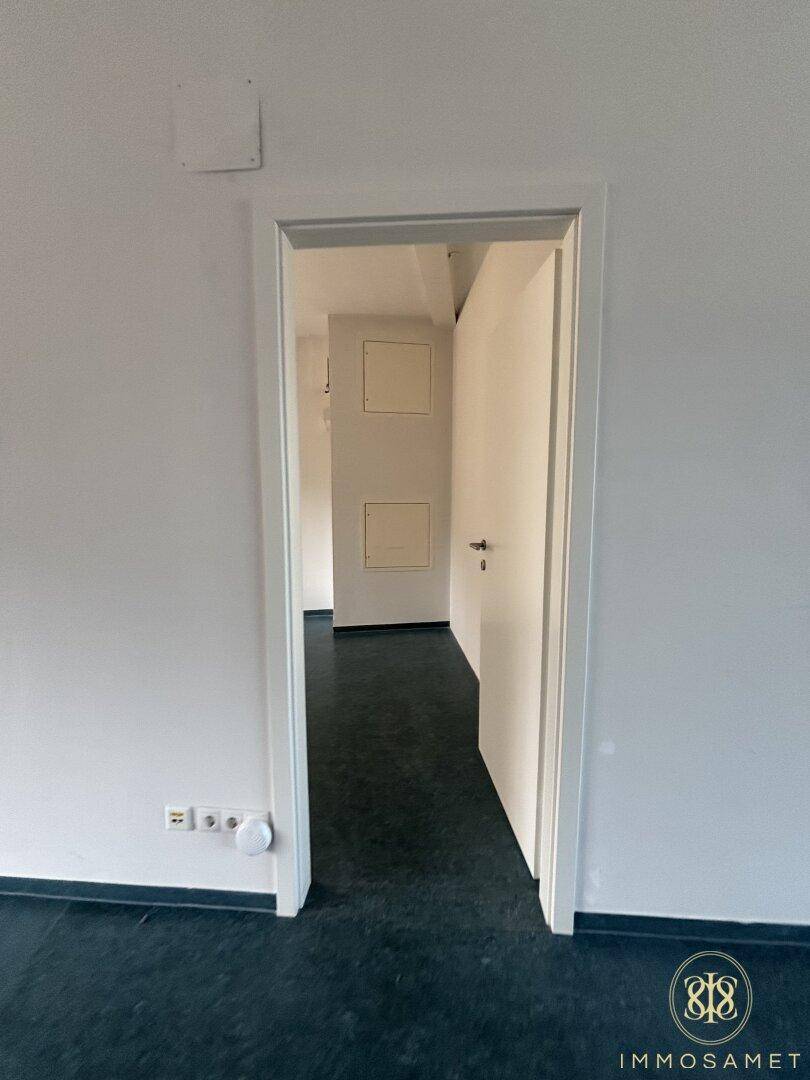 Offener Durchgang zwischen zwei Räumen mit dunklem Bodenbelag und weißen Wänden, schafft eine Verbindung.