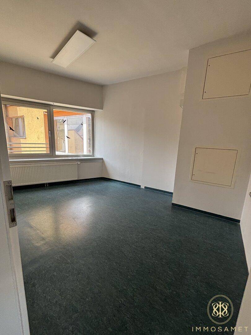 Geräumiger, heller Raum mit dunklem Bodenbelag und Fenster, das Tageslicht hereinlässt und Ausblick bietet.