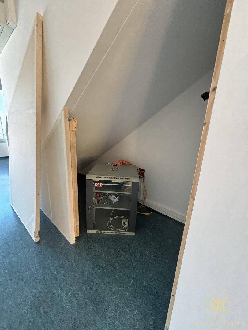 Abstellraum unter der Dachschräge mit technischer Ausrüstung und dunklem Bodenbelag, bietet Stauraum.