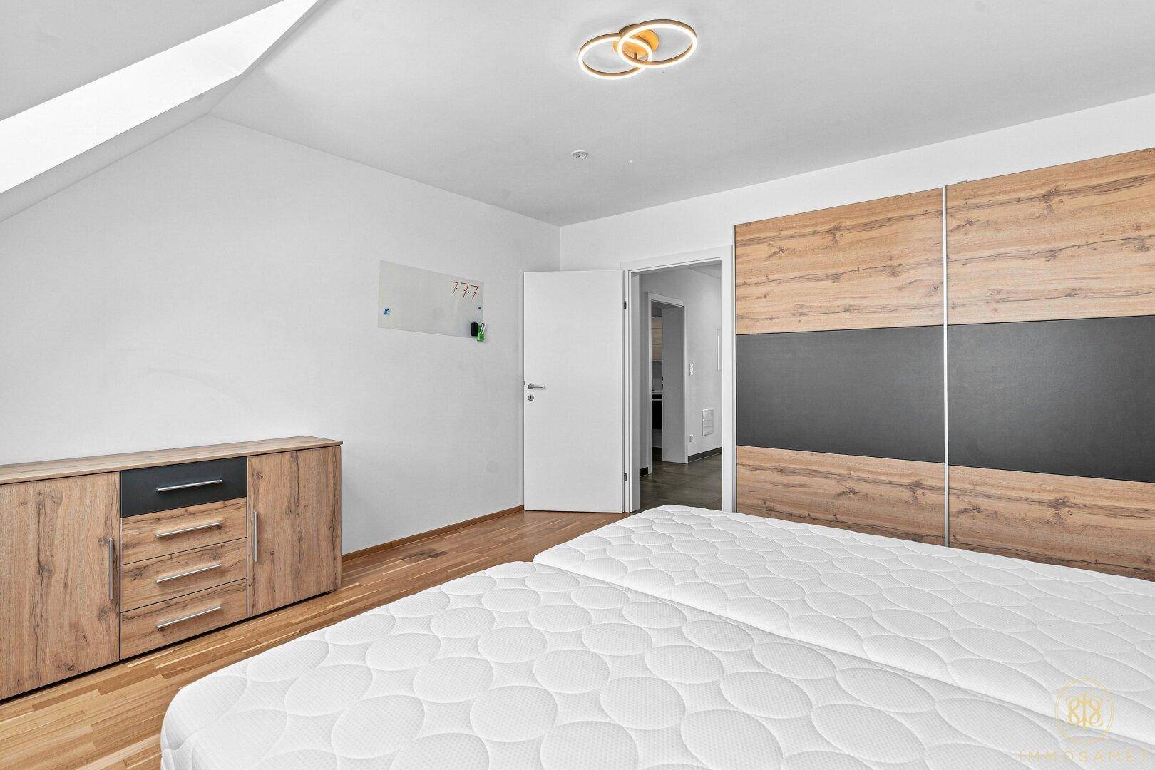 Schlafzimmer mit Holzboden, modernem Einbauschrank und Zugang zu einem weiteren Raum.