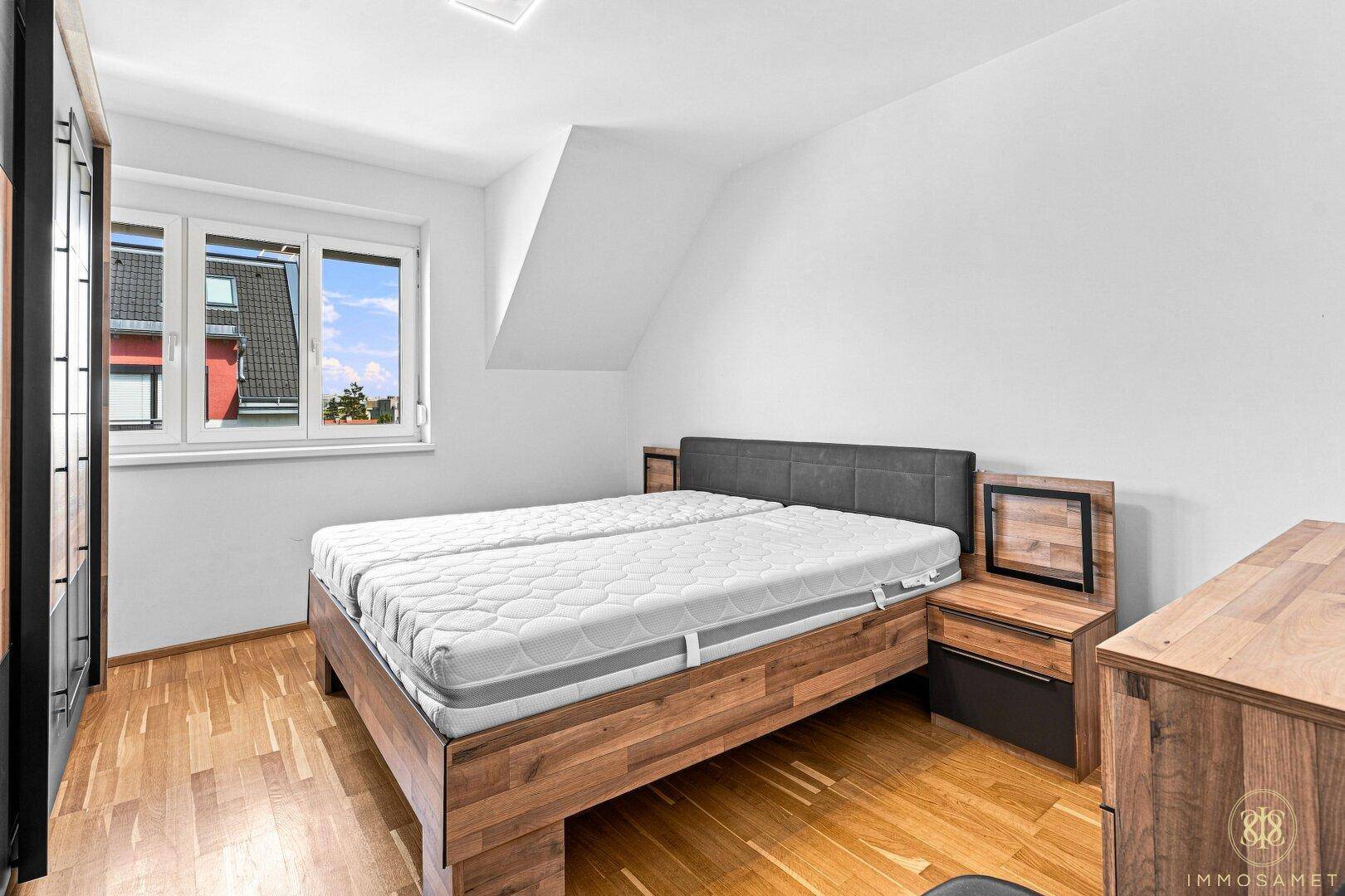 Gemütliches Schlafzimmer mit Holzboden, großem Bett und Fenster mit Blick ins Grüne.