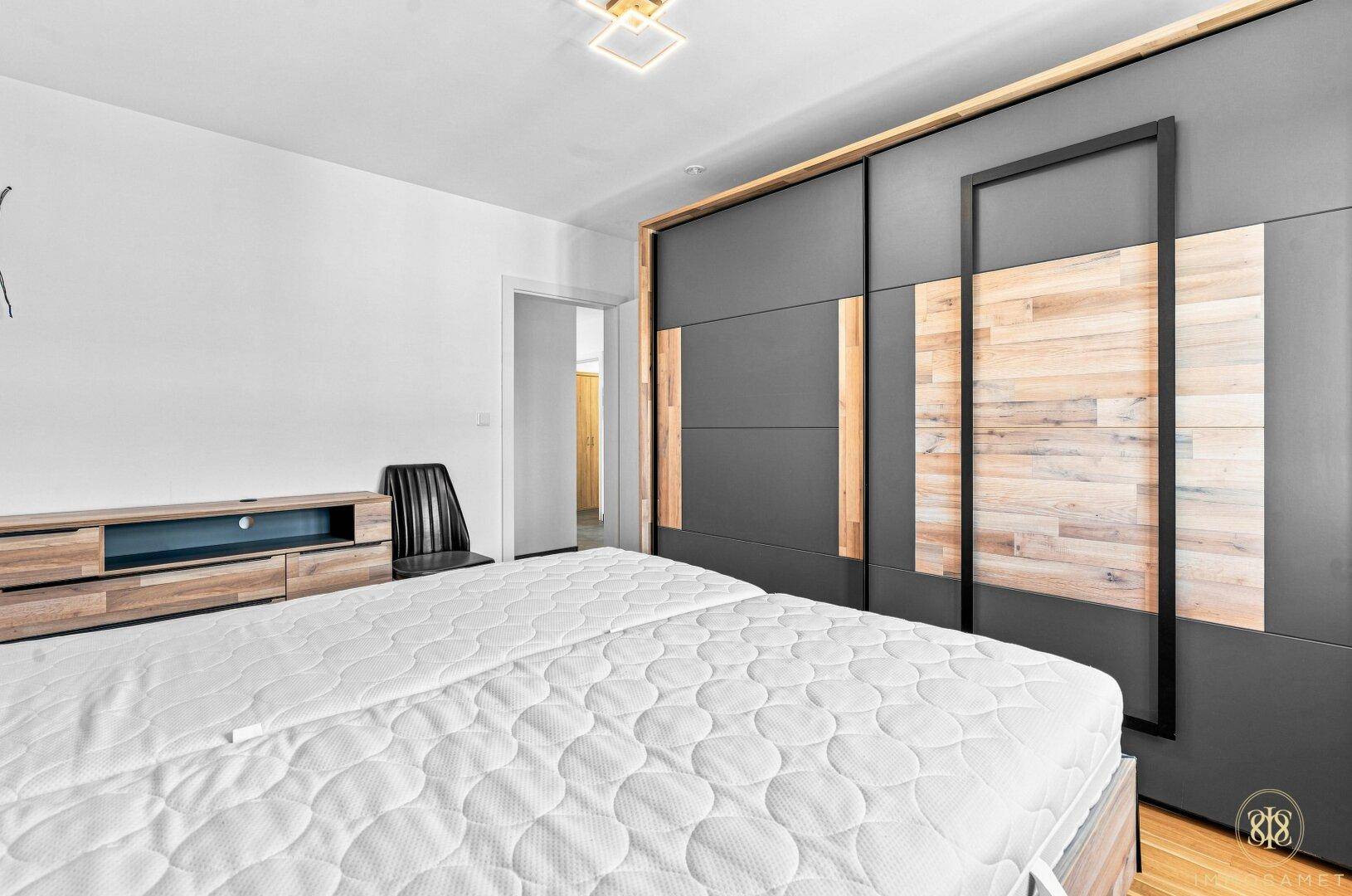 Schlafzimmer mit Holzboden, modernem Schiebetürenschrank und TV-Möbel in Holzoptik.