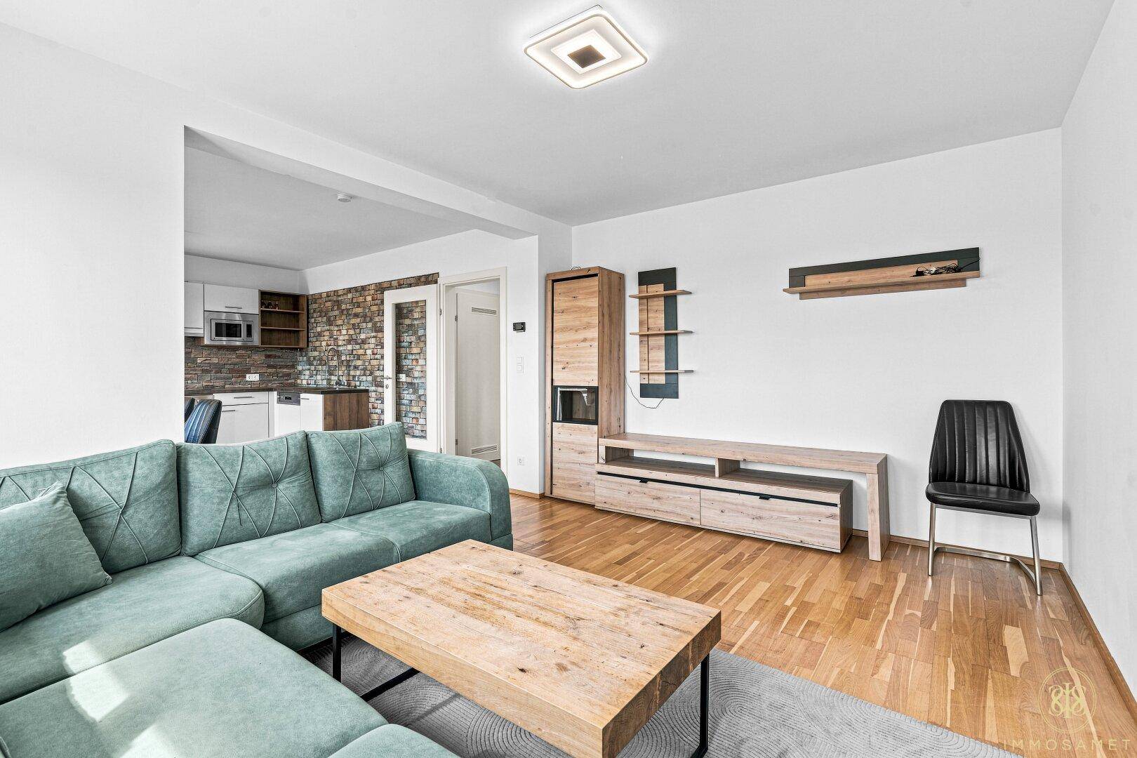Wohnbereich mit grünem Sofa, Holztisch und Blick auf die offene Küche im Hintergrund.