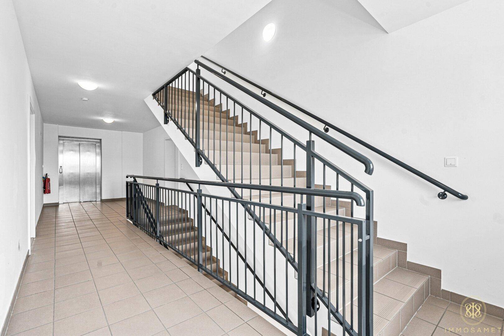 Modernes Treppenhaus mit Geländer und Aufzug im Hintergrund, das alle Etagen verbindet.