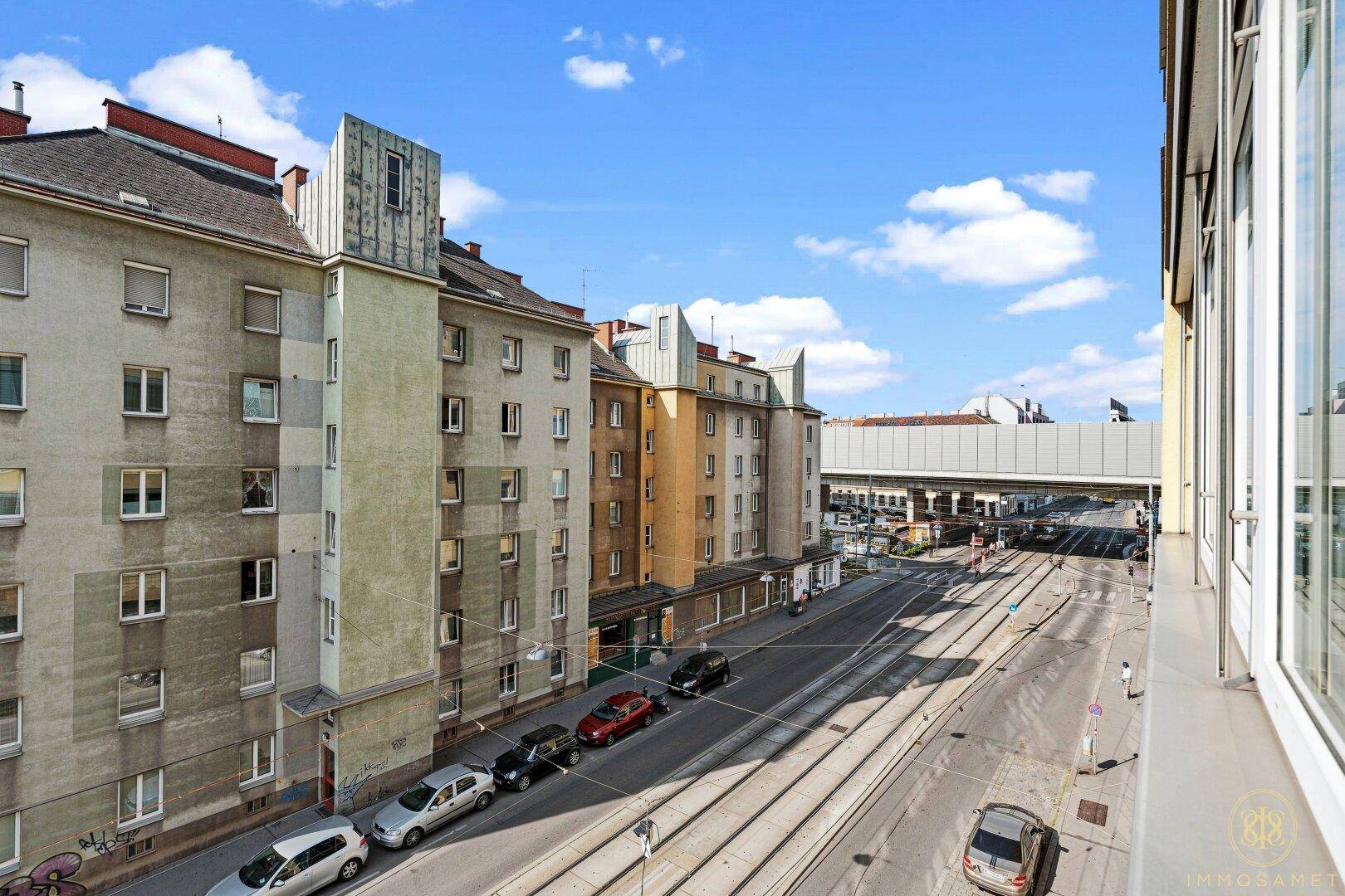 Blick von oben auf eine belebte Straße mit Straßenbahnschienen und älteren Wohngebäuden.