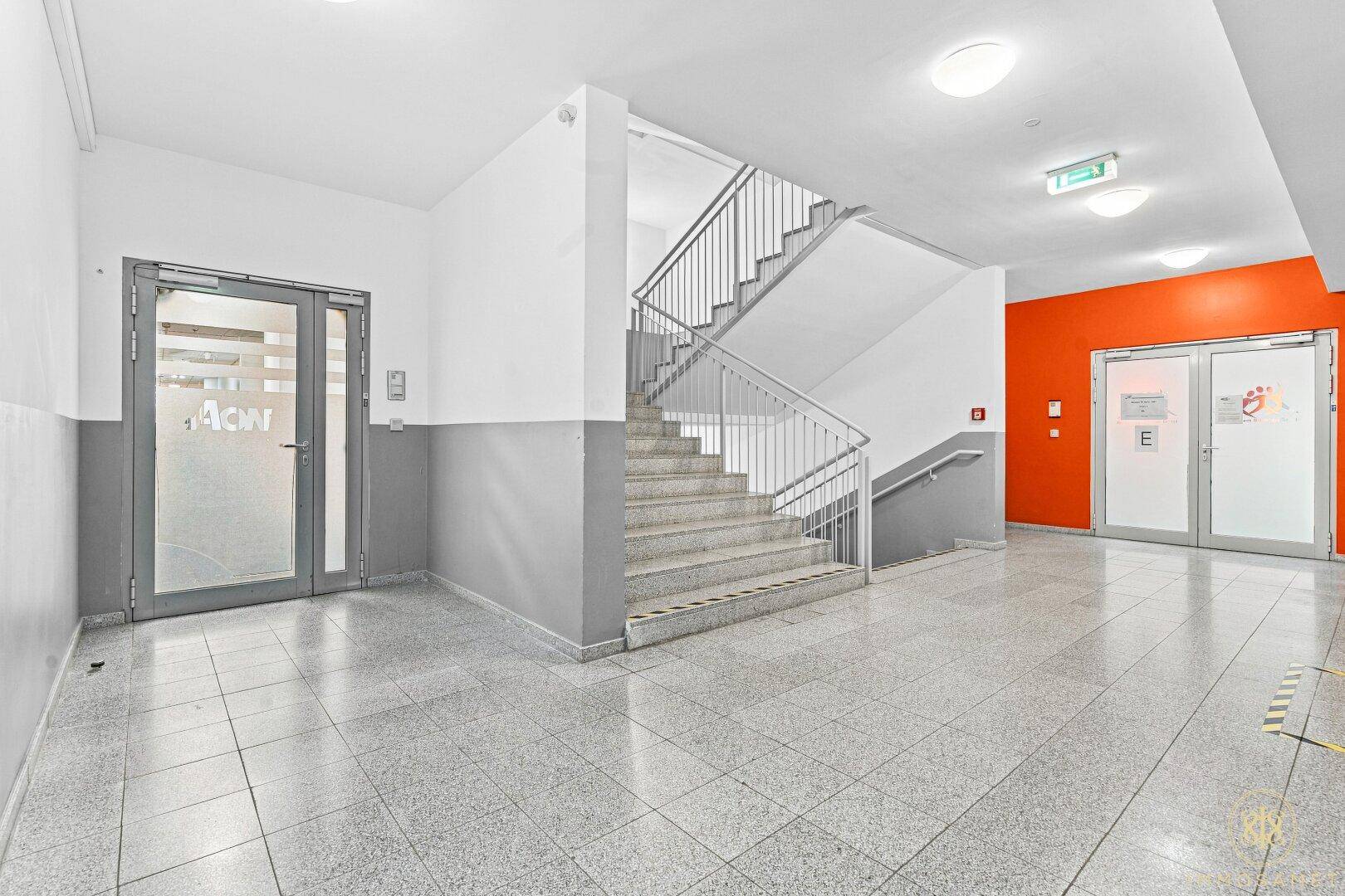 Eingangsbereich mit Treppenhaus, gefliestem Boden und einer leuchtend orangefarbenen Wand.