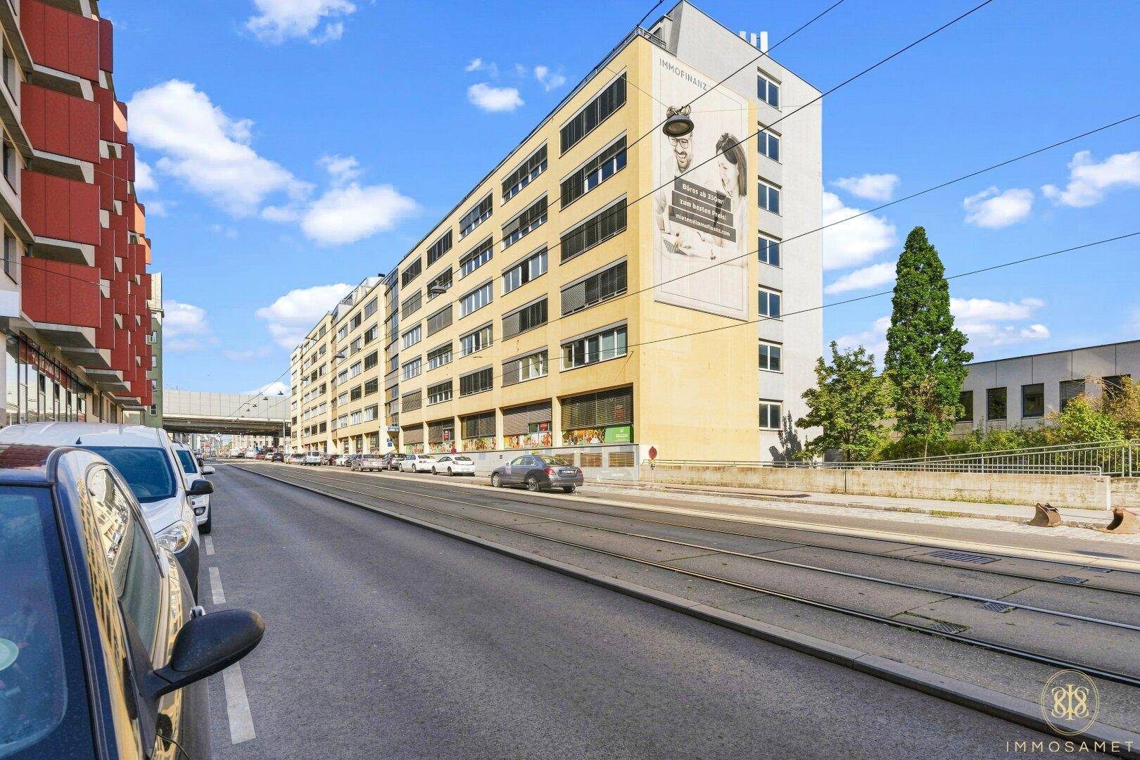Weitläufige Straßenansicht mit dem modernen Geschäftsgebäude und den Straßenbahnschienen.
