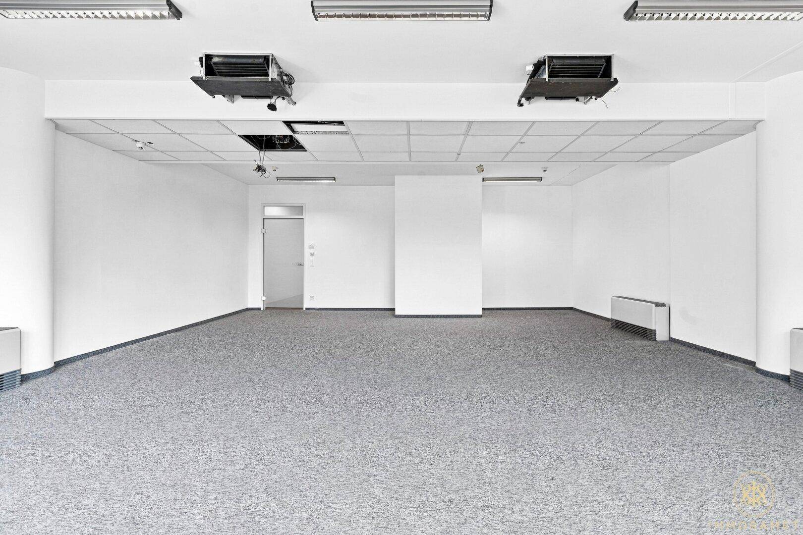 Weiterer Blick in den großen, leeren Büroraum mit Teppichboden und Deckenbeleuchtung.