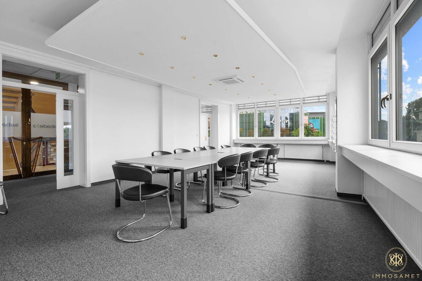 Großer Konferenzraum mit langem Tisch, vielen Stühlen und großen Fenstern für viel Tageslicht.