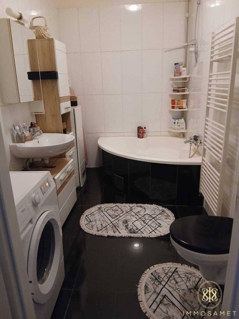Funktionales Badezimmer mit Eckbadewanne, Waschmaschine, Einzelwaschbecken und beheiztem Handtuchhalter.