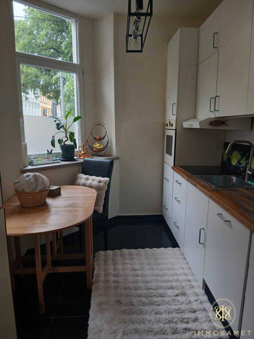 Kleine, helle Küche mit weißer Einbauküche, Holzarbeitsplatte und einem gemütlichen Essbereich am Fenster.
