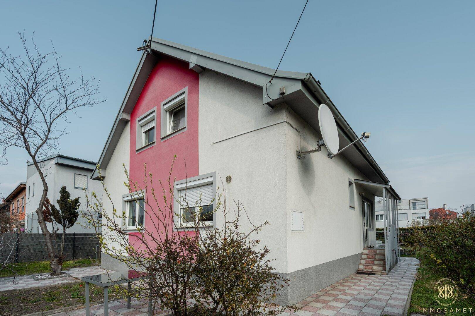 Seitenansicht des Einfamilienhauses mit gepflastertem Weg und schlichtem Design unter blauem Himmel.