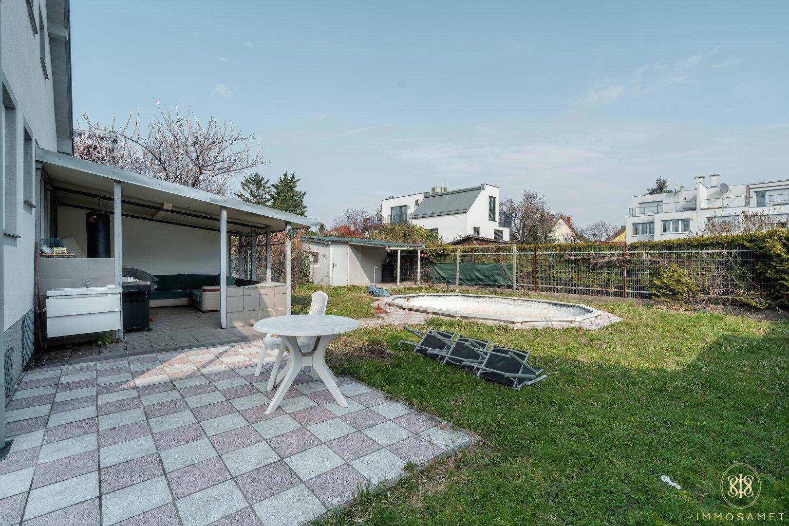 Hinterhof mit gepflasterter Terrasse, überdachtem Sitzbereich, Gartenhaus und einem leeren Pool.
