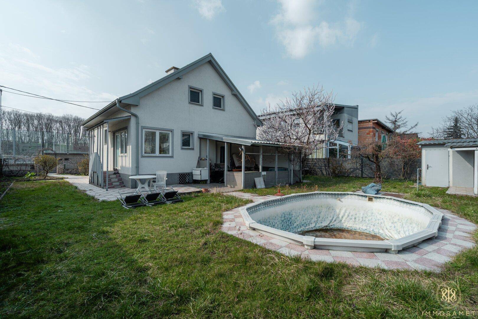 Weitläufiger Gartenbereich hinter dem Haus mit Rasenfläche, einem leeren Pool und umgebender Natur.