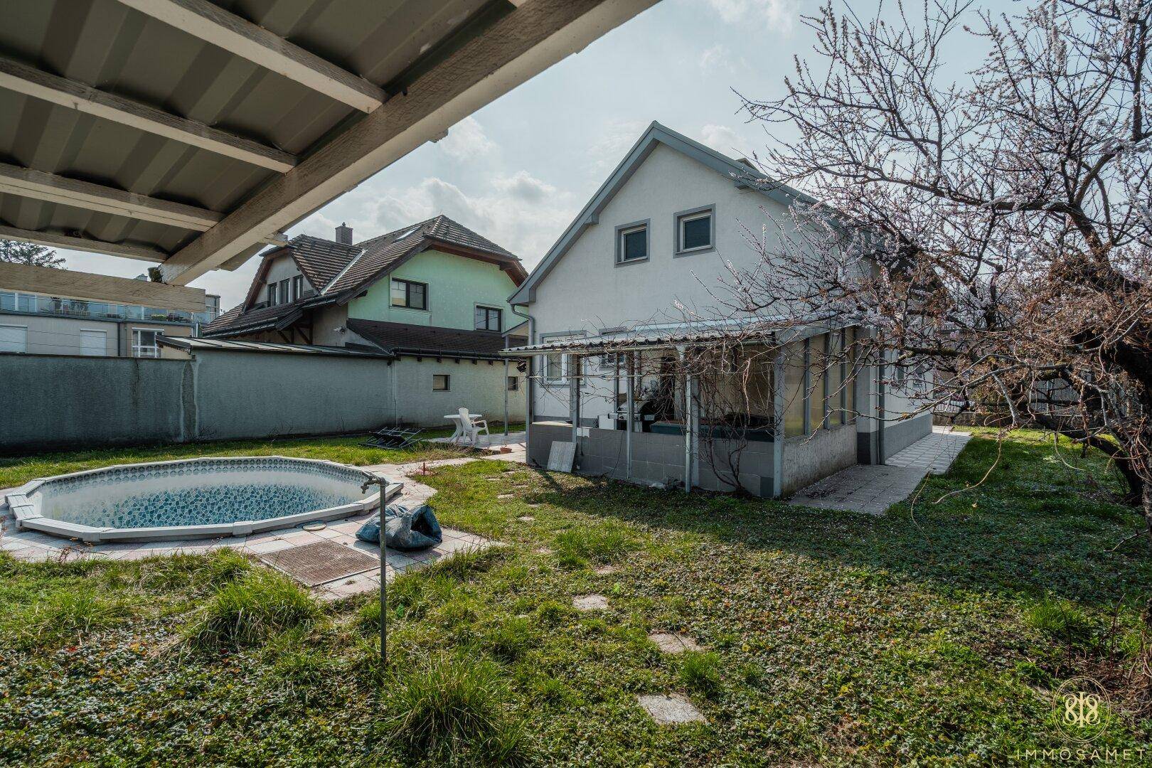Gartenansicht mit teilweise gefülltem Pool, Rasenfläche und dem hinteren Teil des Hauses unter blauem Himmel.
