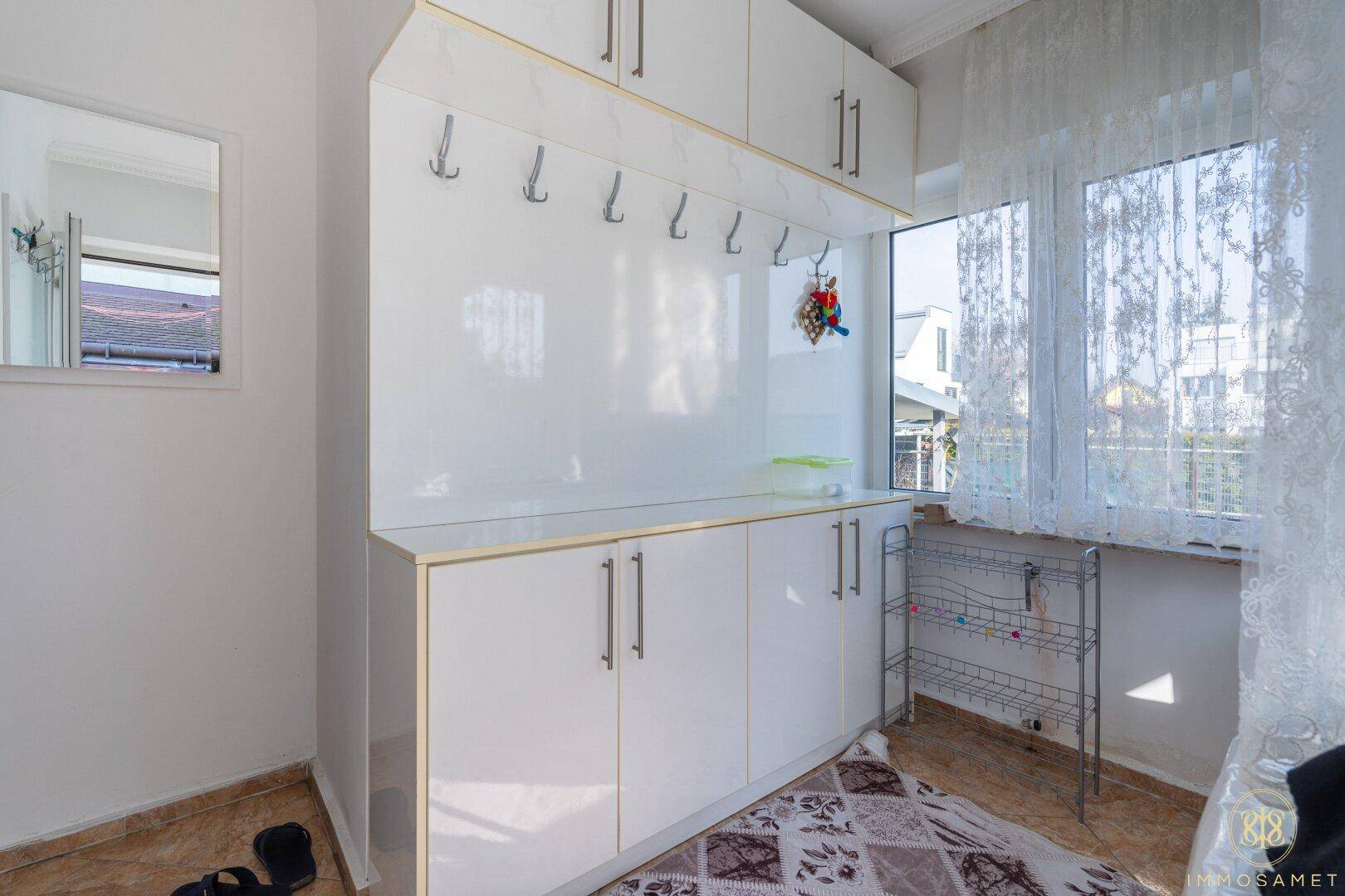 Heller Eingangsbereich mit weißen Einbauschränken, Garderobe und Fenster mit viel Tageslicht.
