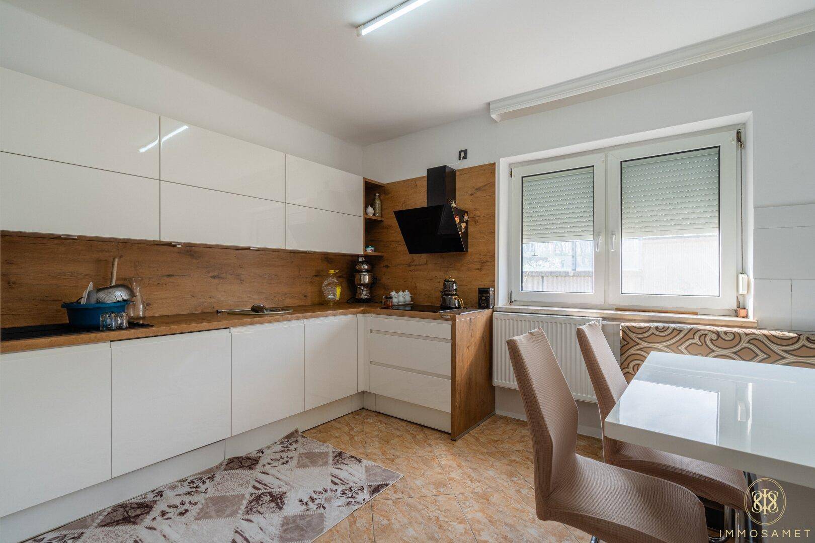 Moderne Küche mit weißen Hochglanzfronten, Holzakzenten und einem gemütlichen Essbereich am Fenster.