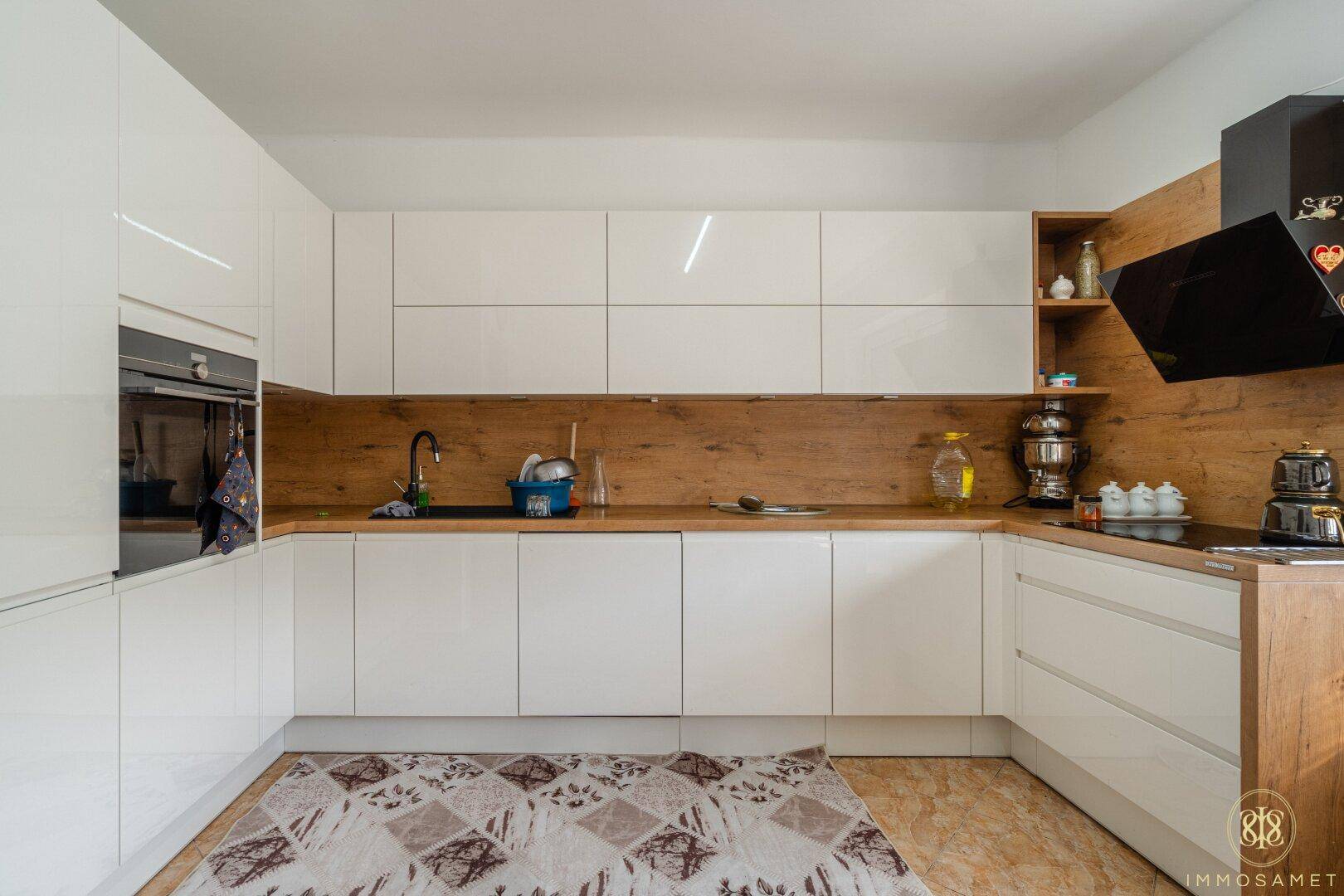Detailansicht der modernen L-förmigen Küche mit weißen Schränken, Holzdetails und integriertem Backofen.