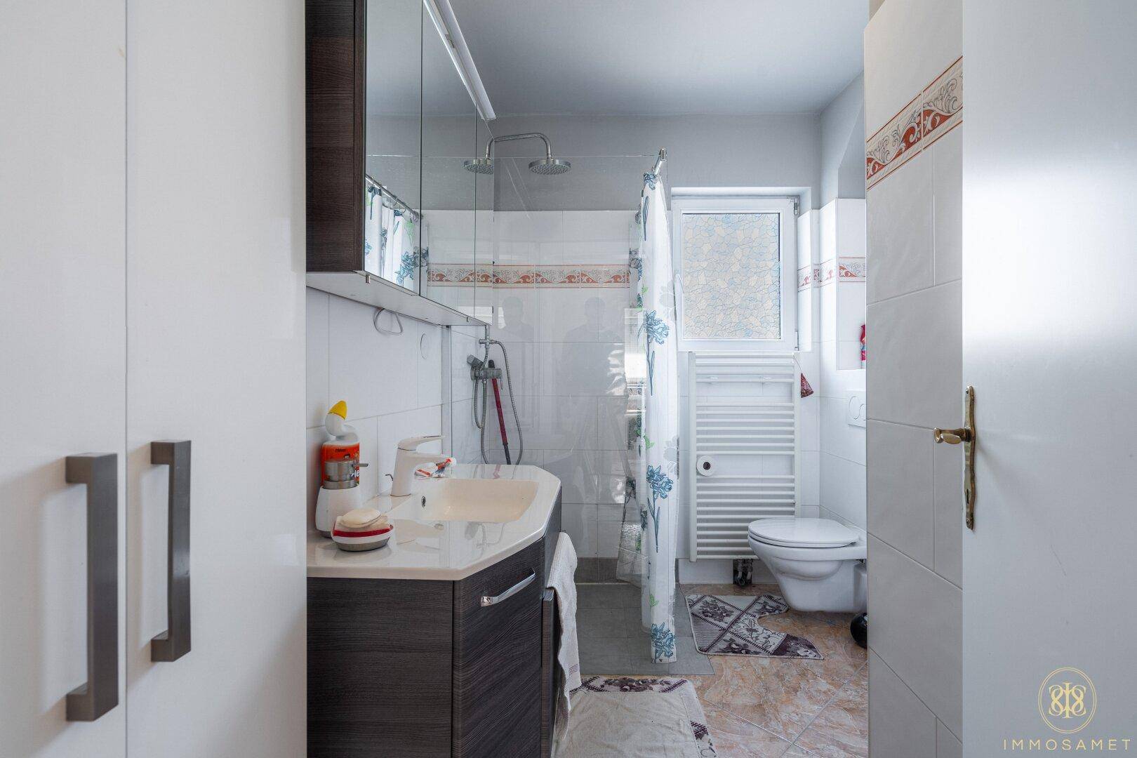 Modernes Badezimmer mit Waschtisch, Spiegelschrank, Dusche, WC und Fenster für natürliche Belüftung.