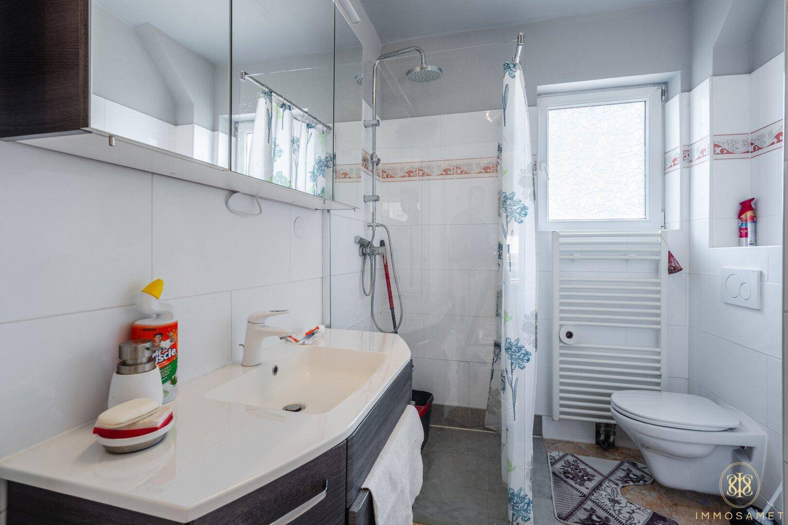 Helles Badezimmer mit Waschtisch, Duschbereich, WC und Fenster für natürliche Belüftung und Licht.
