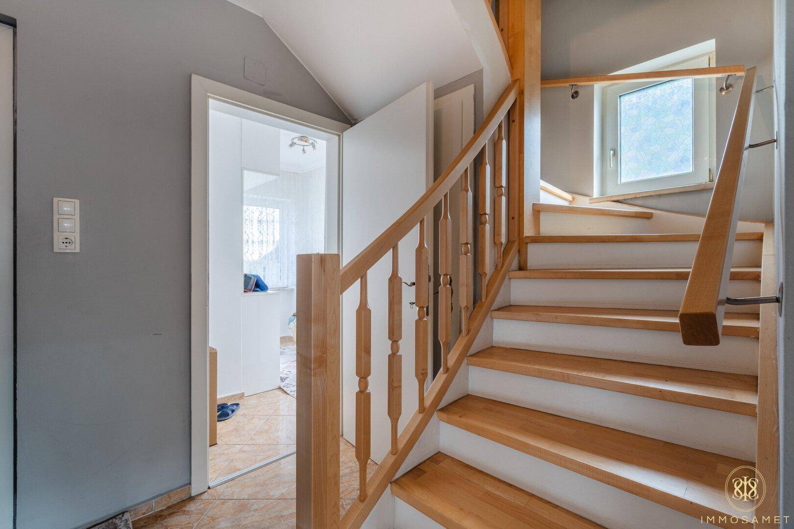 Helle Holztreppe führt in das obere Stockwerk, mit klassischem Geländer und Blick in einen Nebenraum.