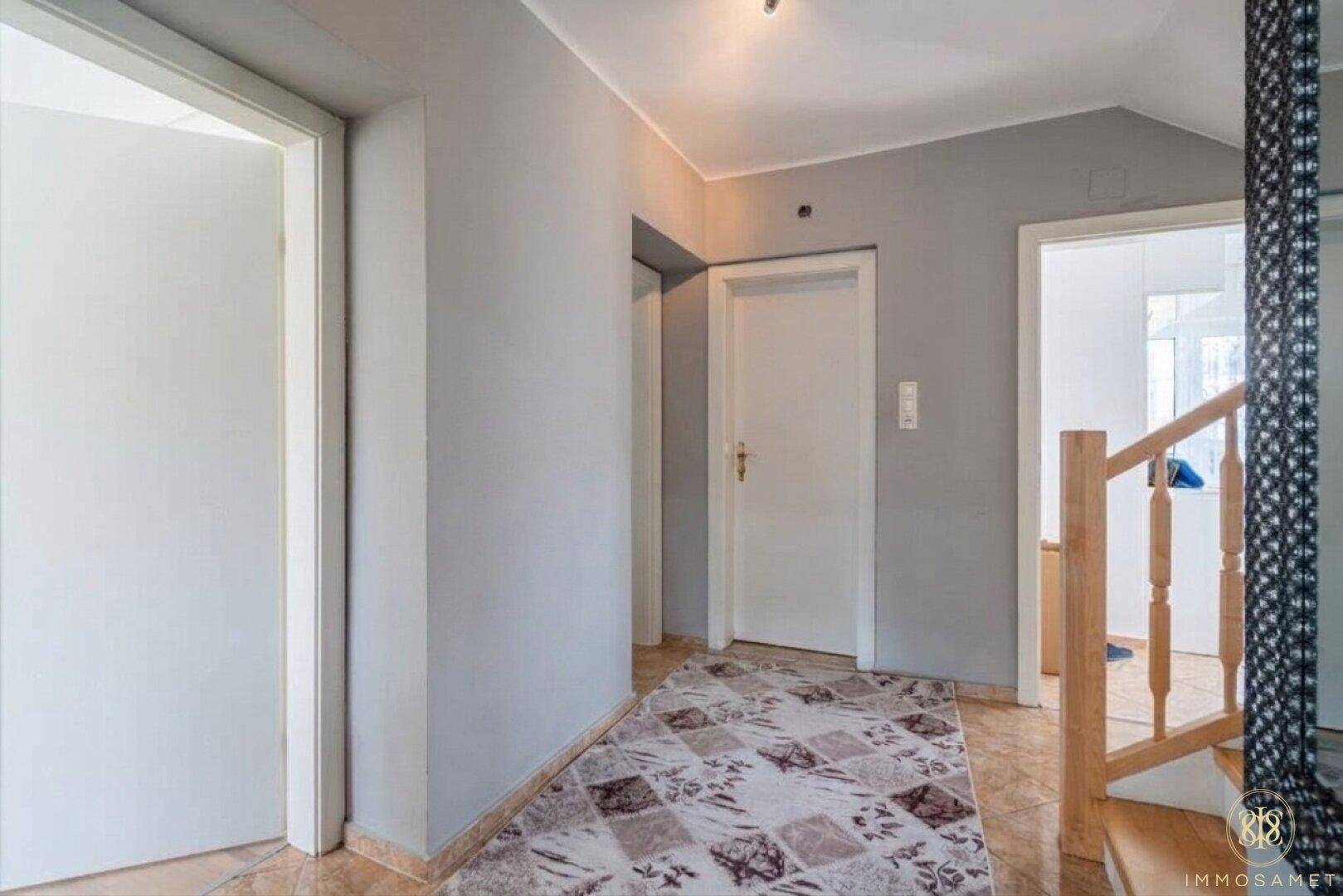 Heller Flur mit grauen Wänden, Fliesenboden und mehreren Türen, die zu den Zimmern führen.