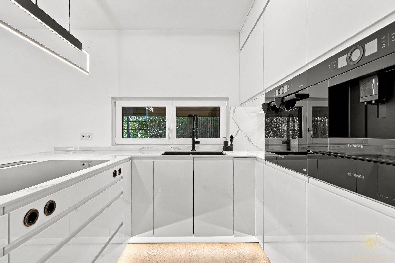 Moderne weiße Küche mit Hochglanzfronten, integrierten Geräten und Fenster.