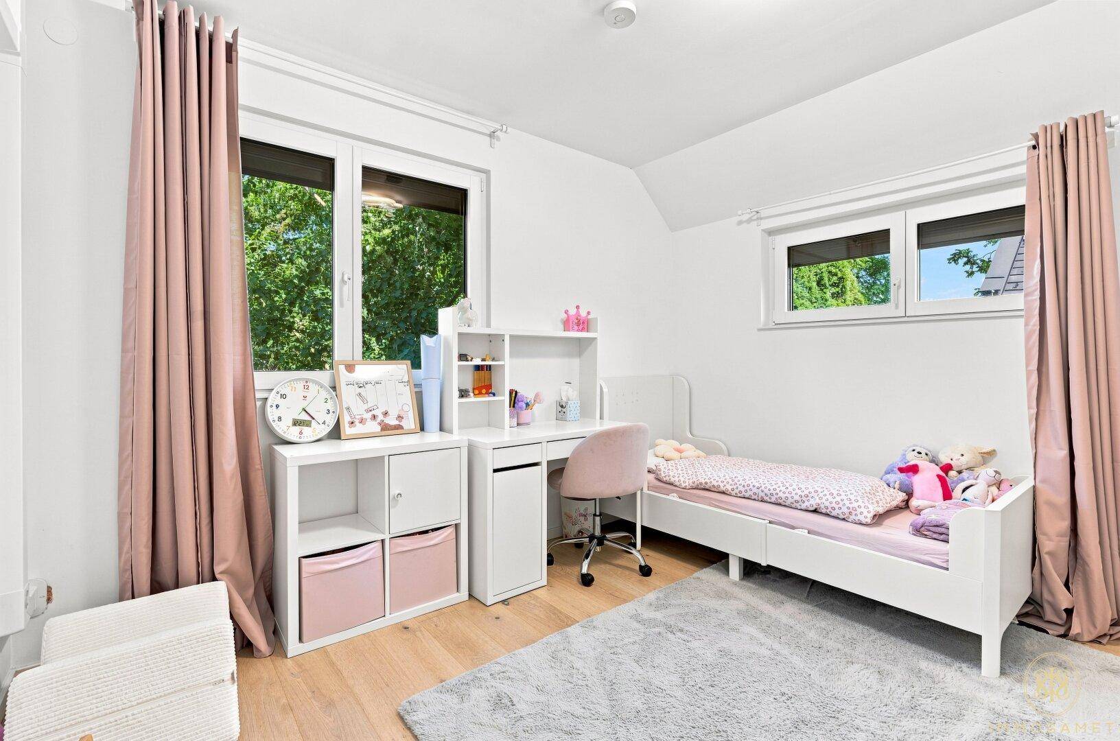 Kinderzimmer mit Schreibtisch, Bett und Blick ins Grüne durch große Fenster.
