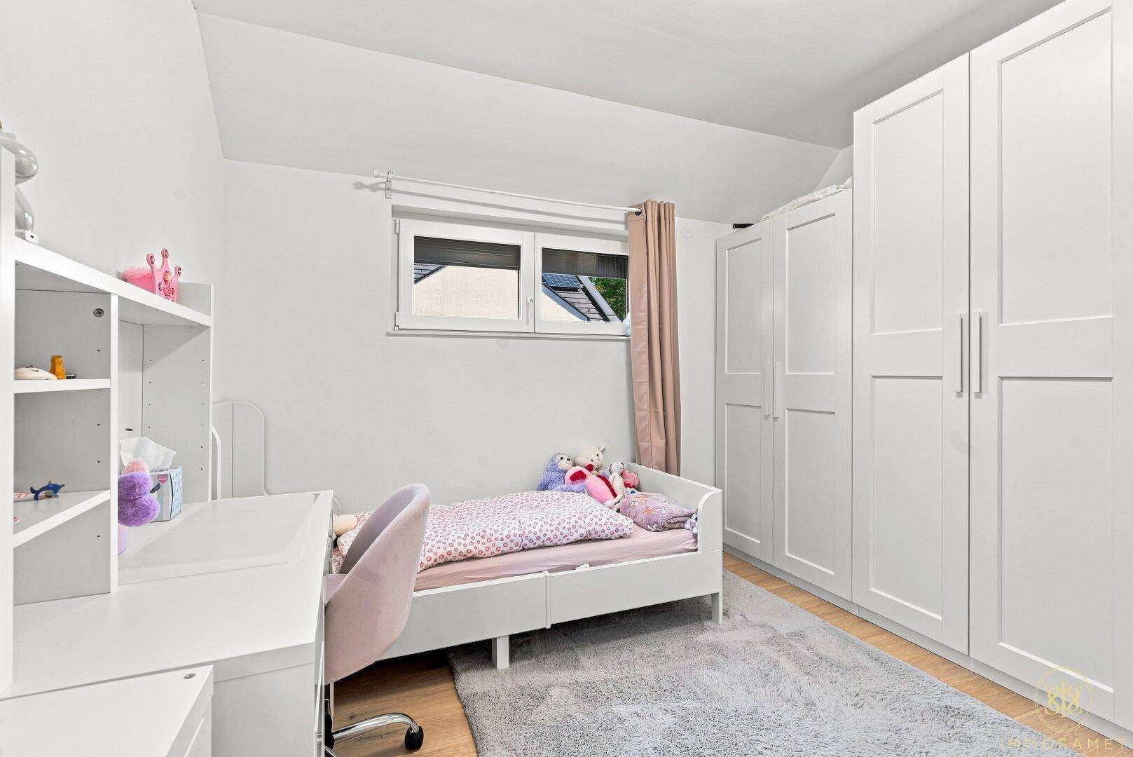 Helles Kinderzimmer mit weißen Schränken, Bett und Schreibtisch.