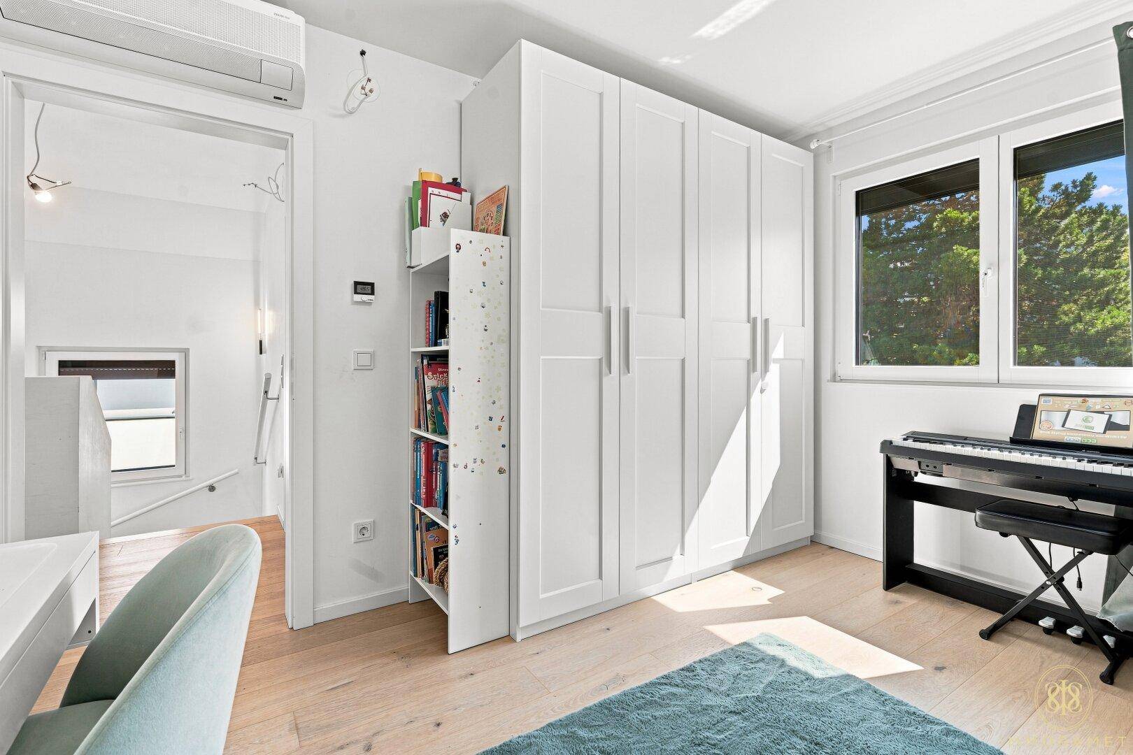 Helles Kinderzimmer mit großen Fenstern, Kleiderschrank und Klavier.