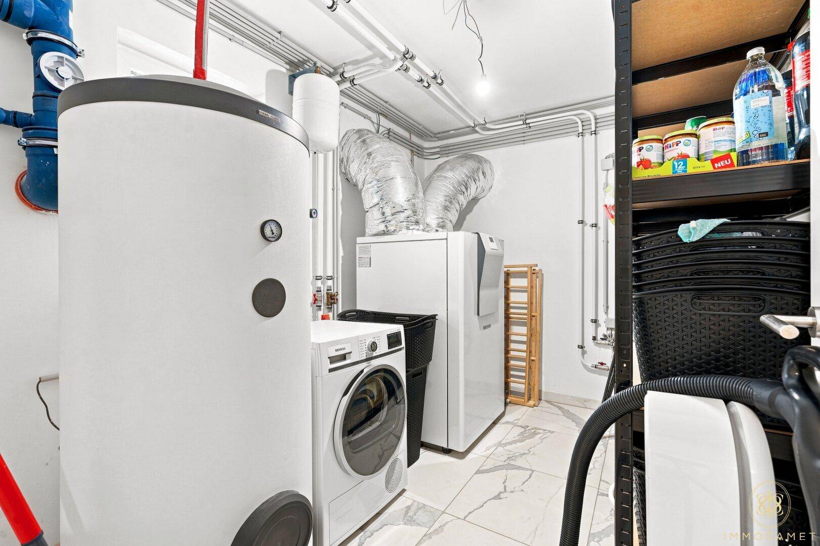 Hauswirtschaftsraum mit Waschmaschine, Trockner, Warmwasserspeicher und sichtbaren Installationen.