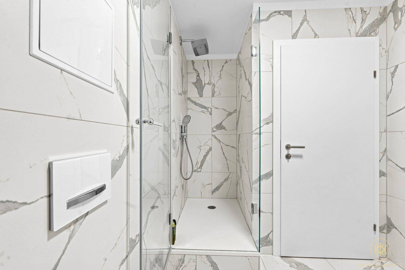 Geräumige Duschkabine mit Glasabtrennung und Regendusche in einem modern gefliesten Badezimmer.
