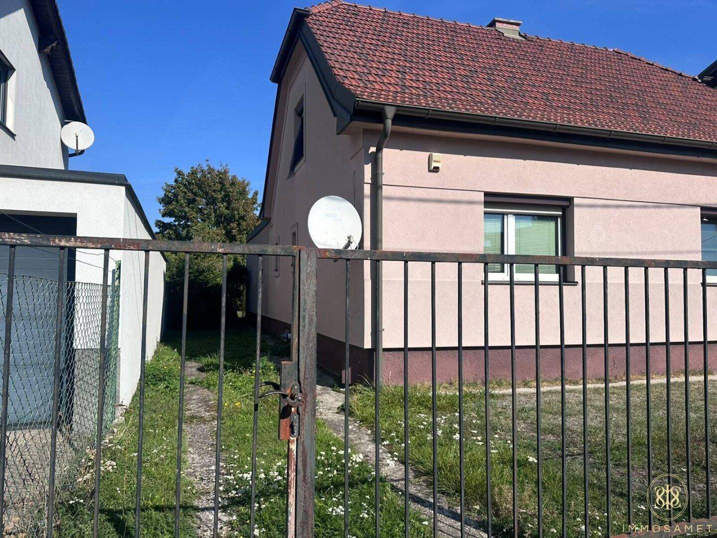 Seitenansicht des Hauses mit rosafarbener Fassade, einem Tor und einer Satellitenschüssel.