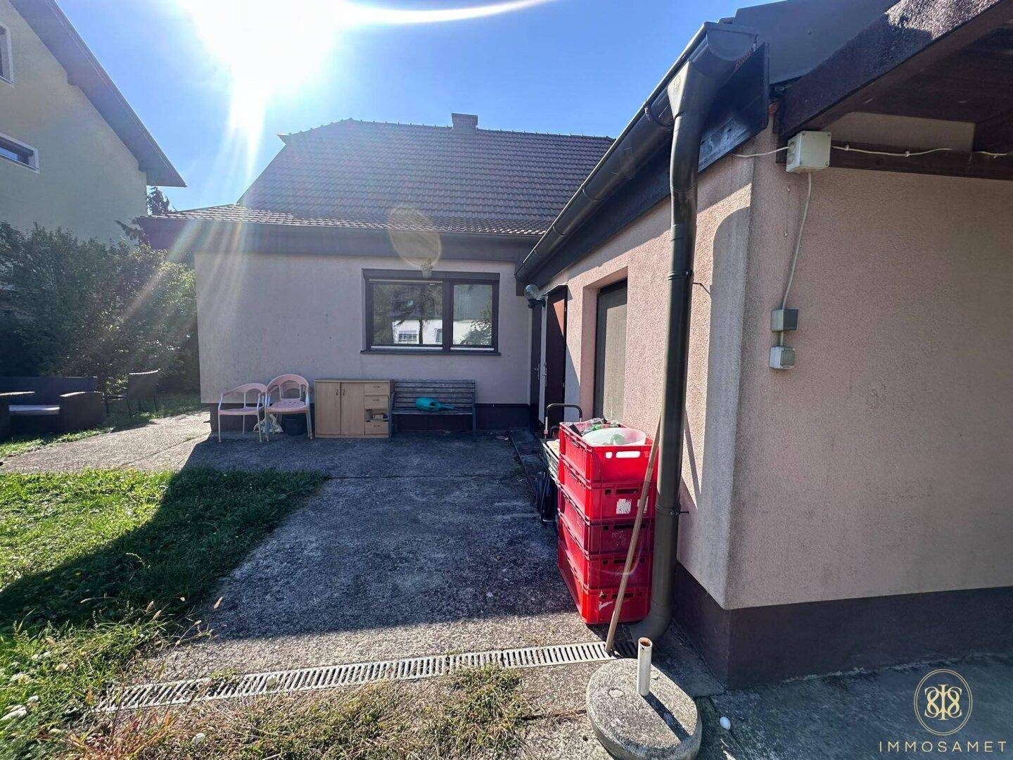 Rückseite des Hauses mit gepflastertem Bereich und Abstellfläche für Gartengeräte.
