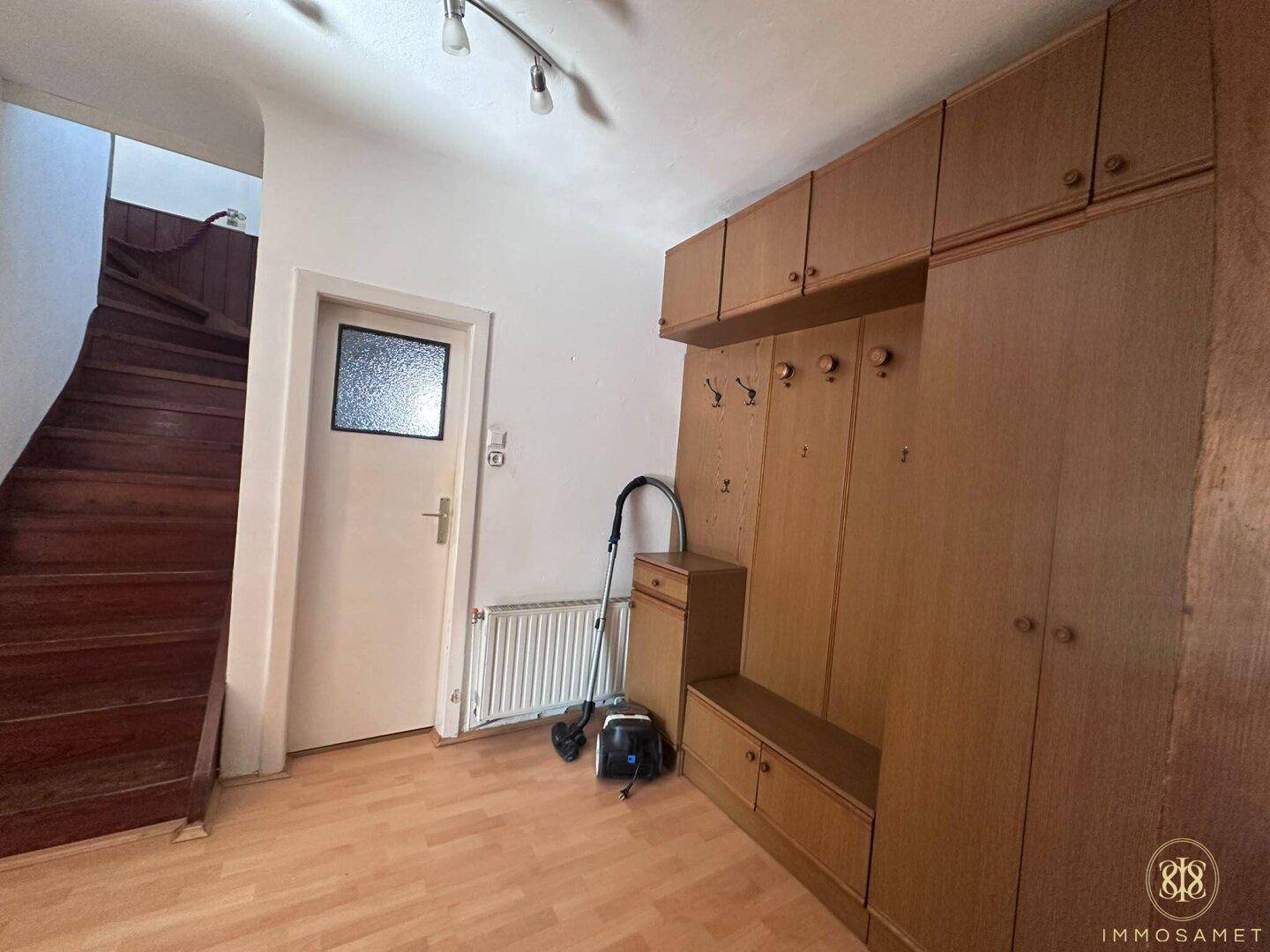 Geräumiger Flur mit Holztreppe, Heizkörper und großem Einbauschrank.