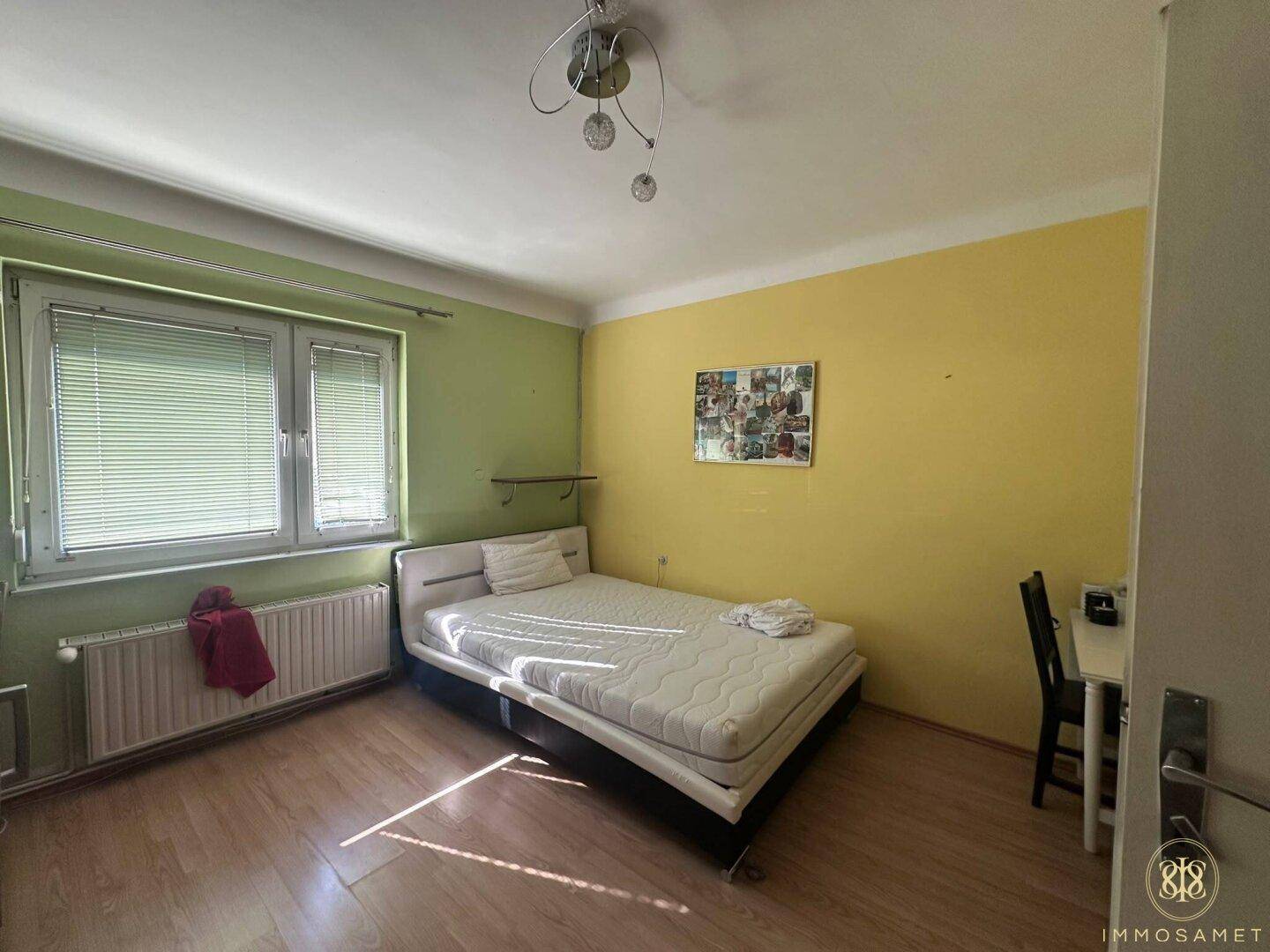 Schlafzimmer mit hellem Laminatboden und farbigen Wänden, bietet Platz für ein Bett und einen Schreibtisch.
