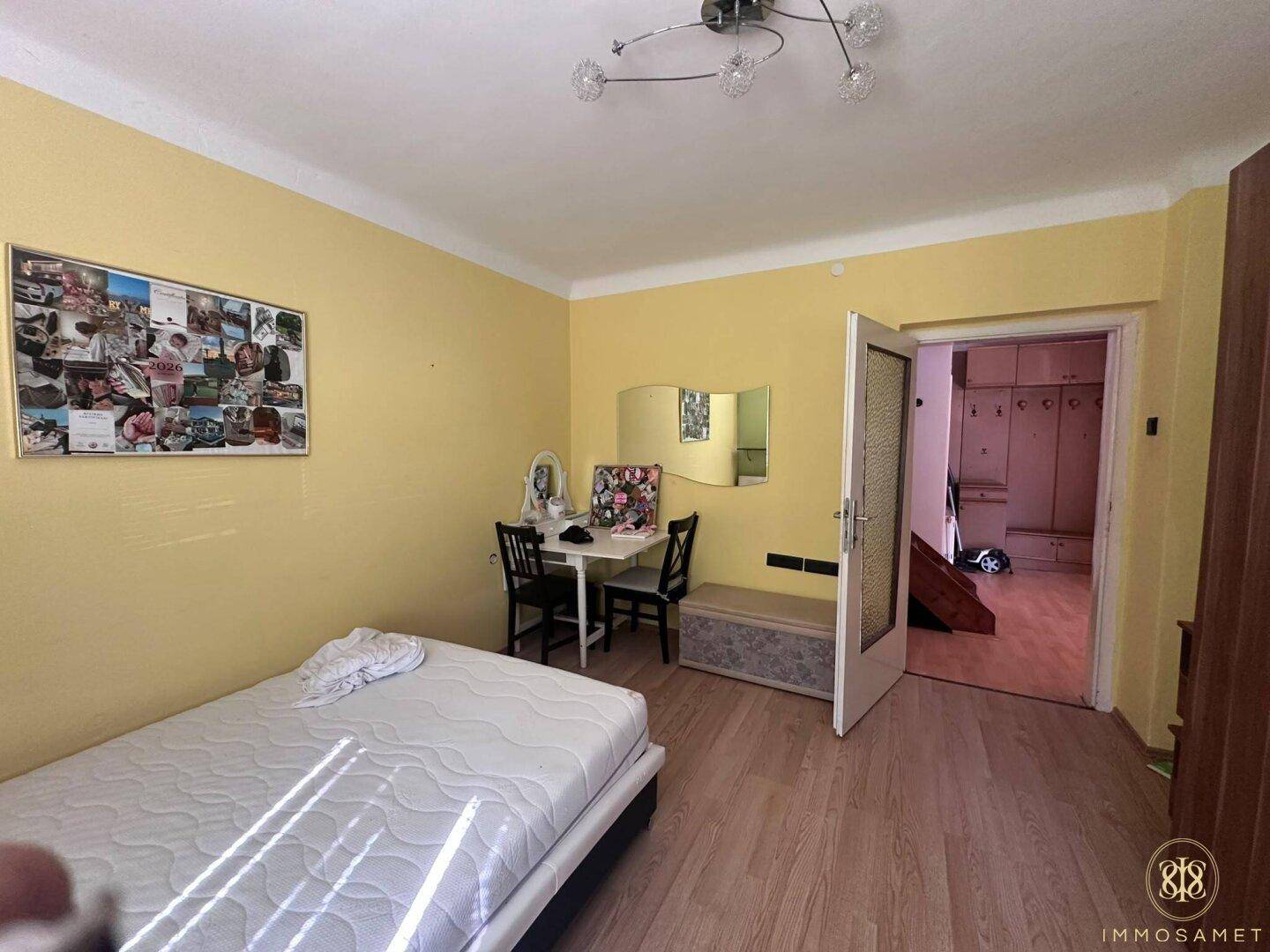 Schlafzimmer mit Laminatboden und gelben Wänden, ausgestattet mit Bett und Schminktisch.