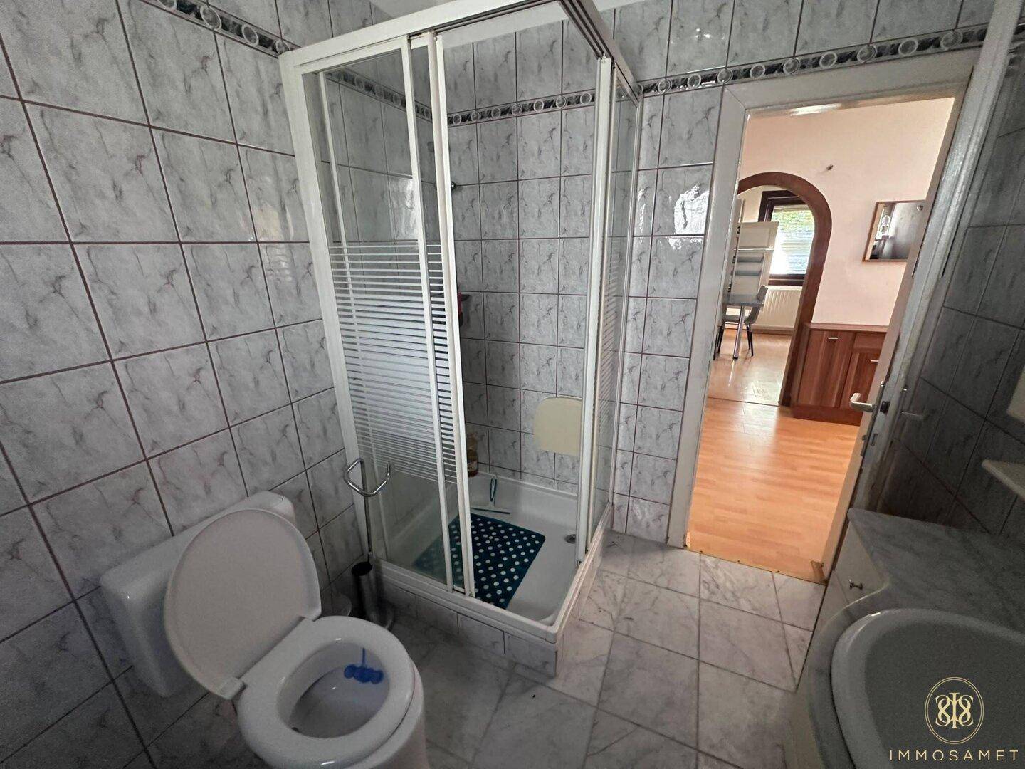 Badezimmer mit Fliesenboden, Duschkabine und WC, in einem älteren, funktionalen Zustand.