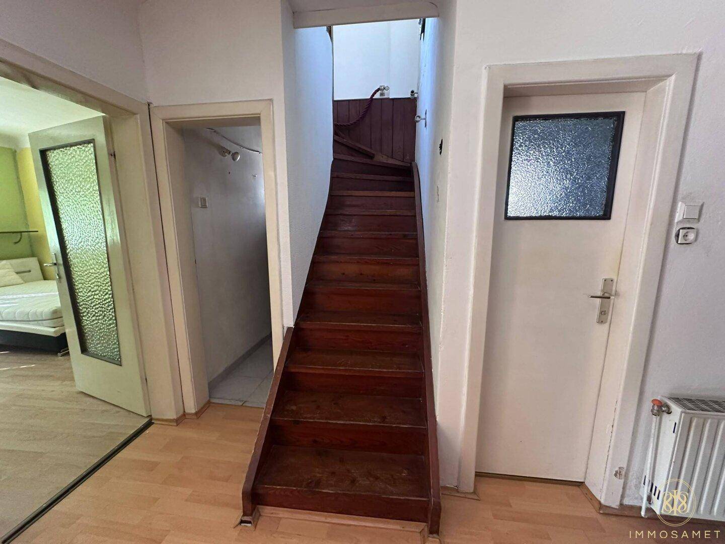 Flur mit Holztreppe zum Obergeschoss und Zugang zu verschiedenen Zimmern, funktional gestaltet.
