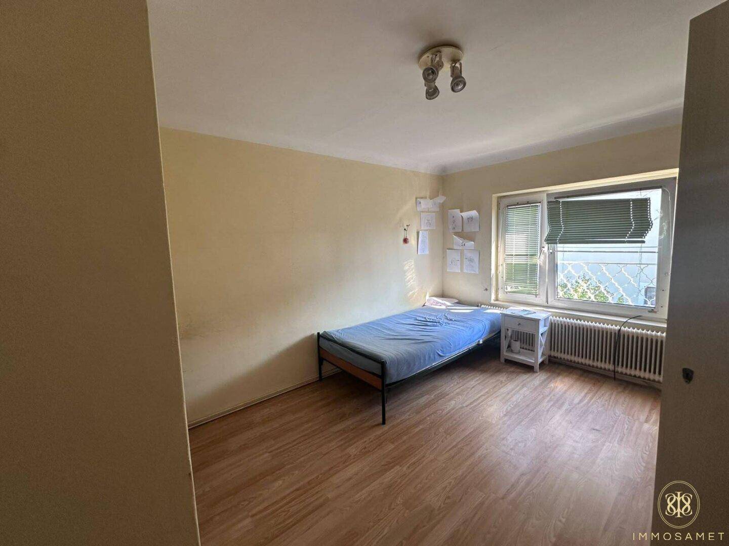 Helles Schlafzimmer mit Einzelbett und Laminatboden, ausgestattet mit einem Fenster für Tageslicht.